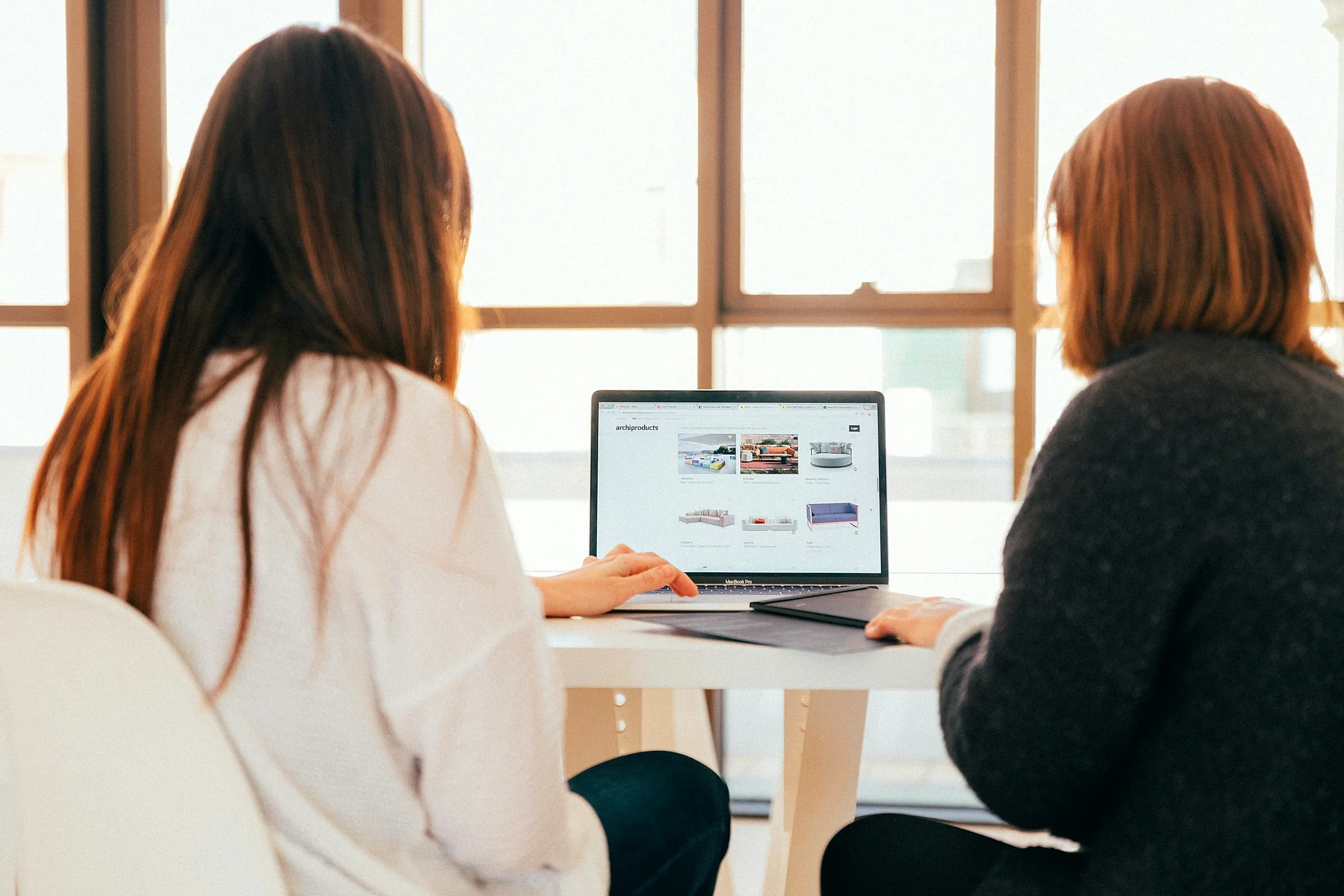 Two colleagues talk over a laptop screen at a shared desk