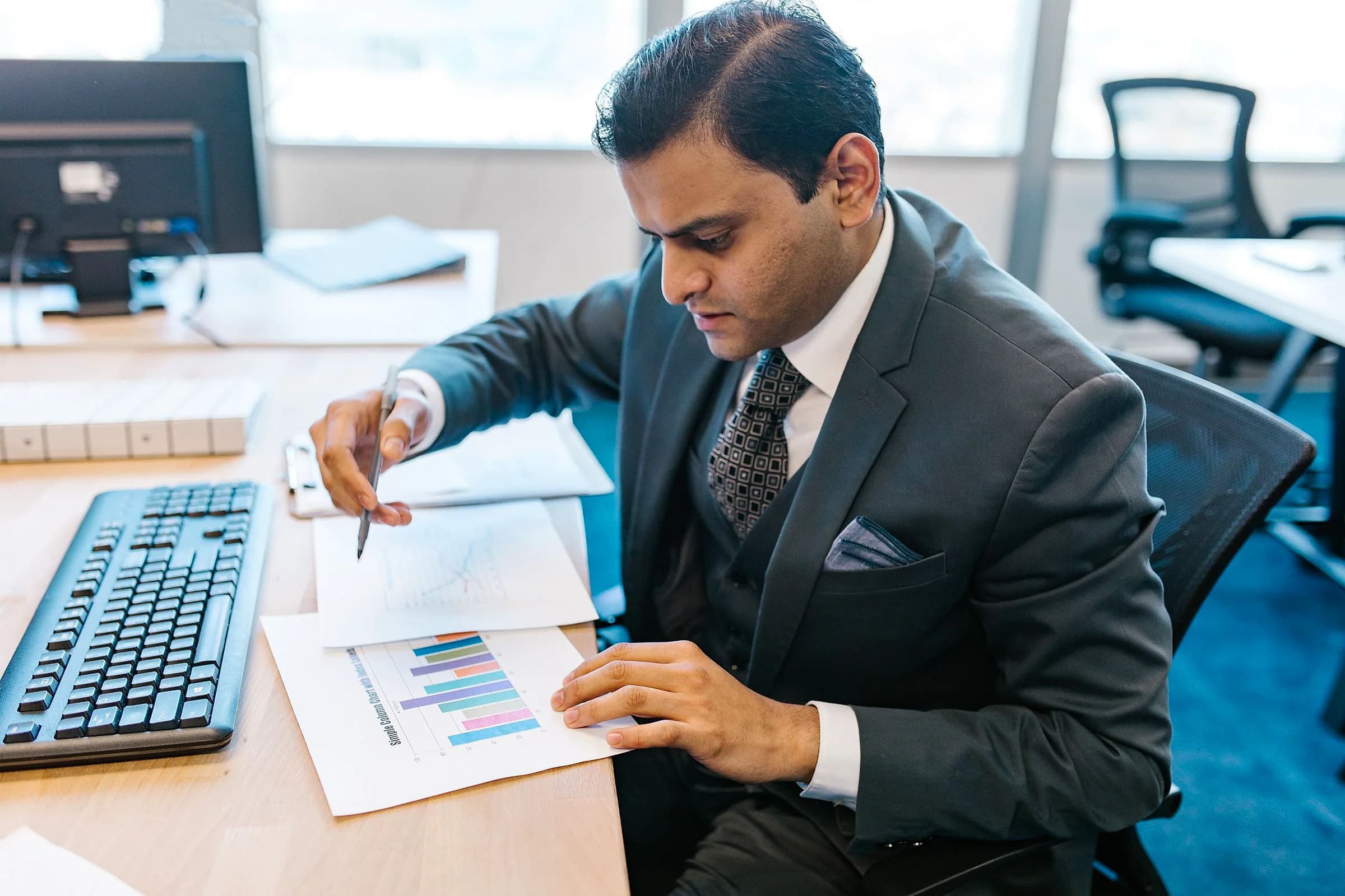 A man in a grey suit annotates a printed chart at his desk